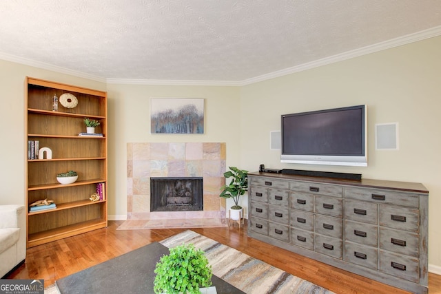 living area with crown molding, wood finished floors, a textured ceiling, and a tiled fireplace