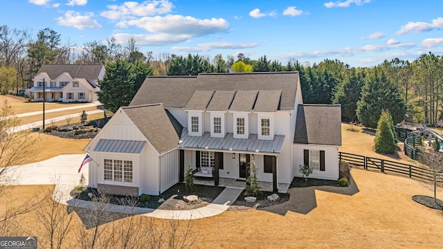 modern farmhouse featuring fence, board and batten siding, covered porch, a standing seam roof, and metal roof
