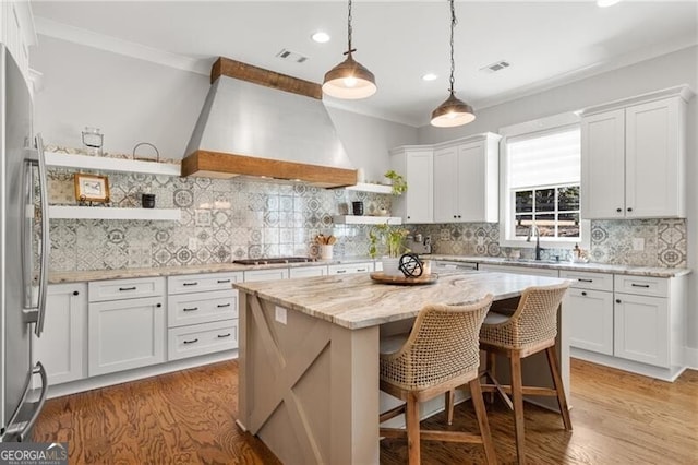 kitchen featuring open shelves, custom exhaust hood, freestanding refrigerator, a center island, and crown molding