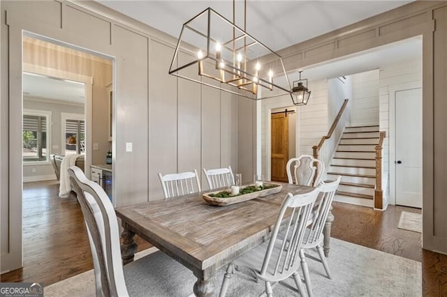 dining room featuring wood finished floors, stairs, a chandelier, and a decorative wall