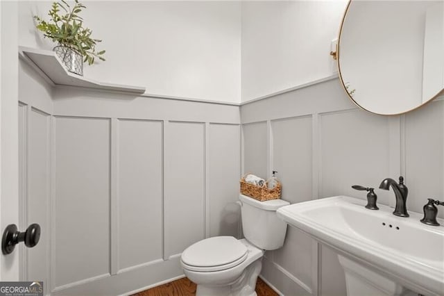 half bathroom with a sink, a decorative wall, toilet, and wood finished floors
