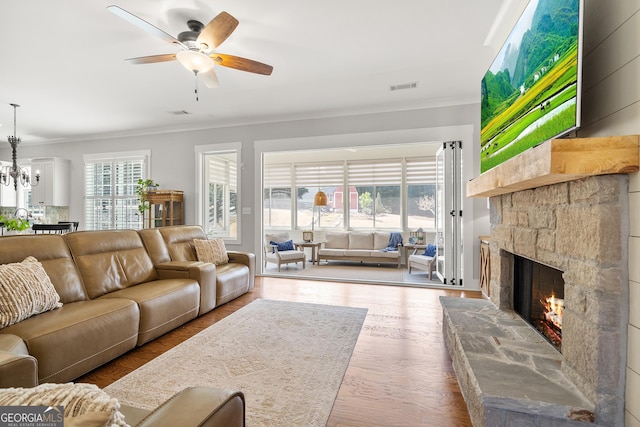 living area featuring ornamental molding, a ceiling fan, a stone fireplace, a chandelier, and wood finished floors