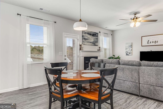 dining area with a ceiling fan, wood finished floors, a fireplace, and visible vents