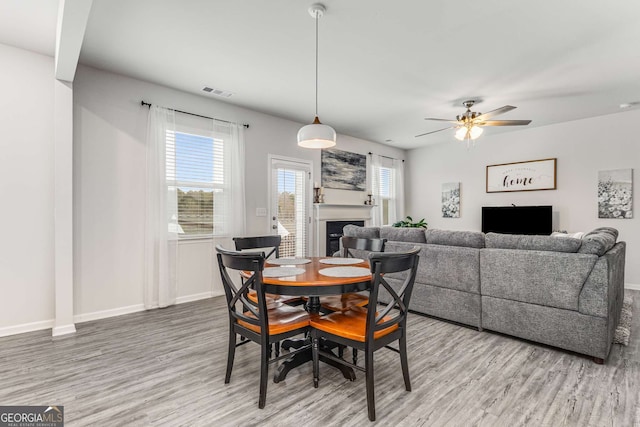 dining space featuring a ceiling fan, a fireplace, wood finished floors, baseboards, and visible vents