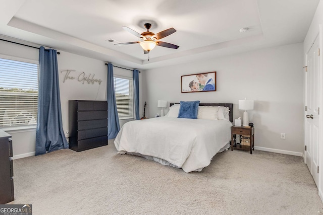 bedroom featuring a raised ceiling, light carpet, baseboards, and ceiling fan