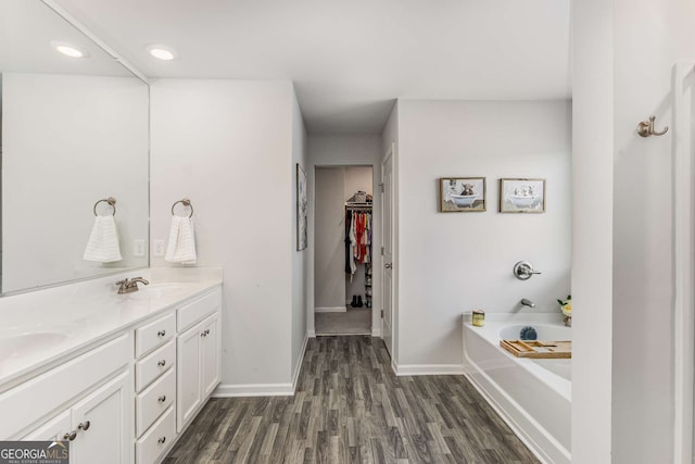 full bathroom with wood finished floors, baseboards, a sink, double vanity, and a bath