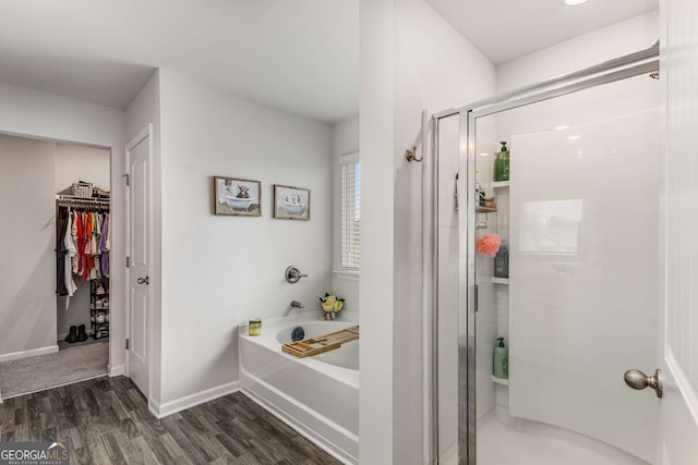 full bathroom featuring a walk in closet, baseboards, a stall shower, a garden tub, and wood finished floors
