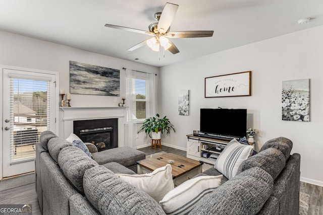 living area featuring baseboards, visible vents, a ceiling fan, a glass covered fireplace, and wood finished floors