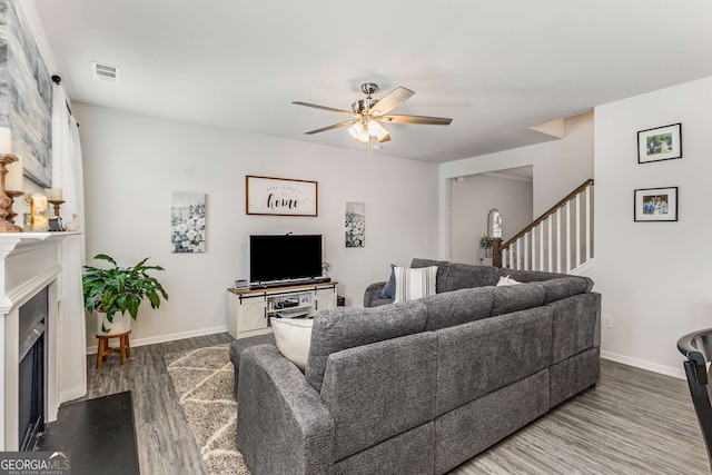 living area featuring a fireplace, wood finished floors, baseboards, visible vents, and ceiling fan