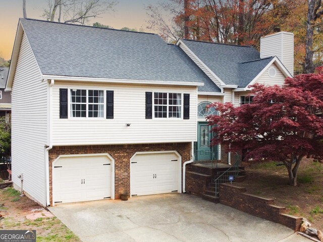 raised ranch with brick siding, driveway, a shingled roof, and a garage