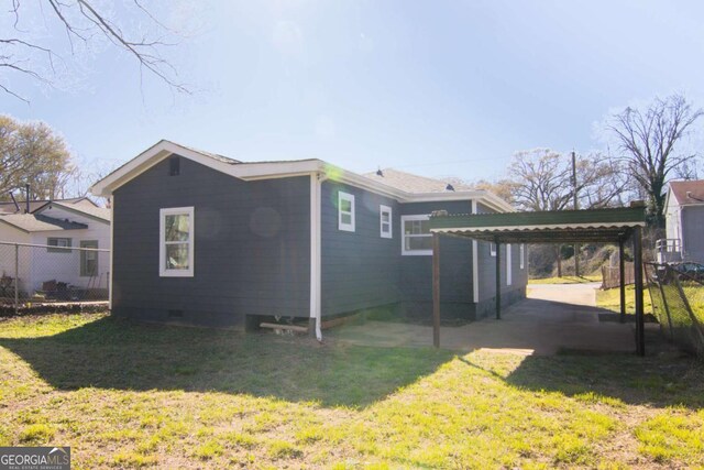back of property with crawl space, a detached carport, a yard, and fence