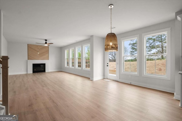 unfurnished living room with visible vents, a glass covered fireplace, light wood-style floors, baseboards, and ceiling fan