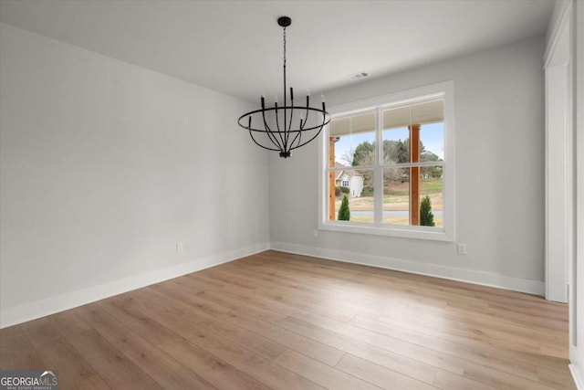 unfurnished dining area with light wood-type flooring, visible vents, baseboards, and a notable chandelier