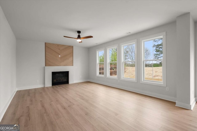 unfurnished living room with a ceiling fan, a fireplace, baseboards, and light wood finished floors
