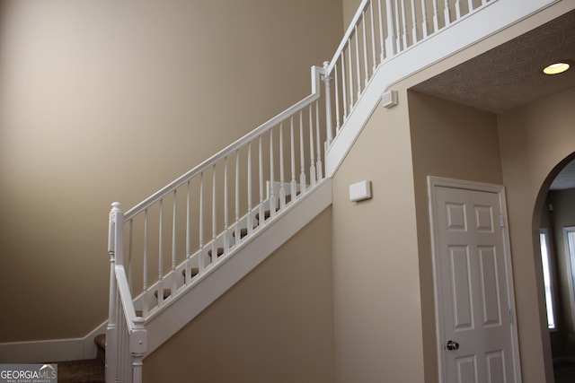 stairs featuring baseboards, arched walkways, and a towering ceiling