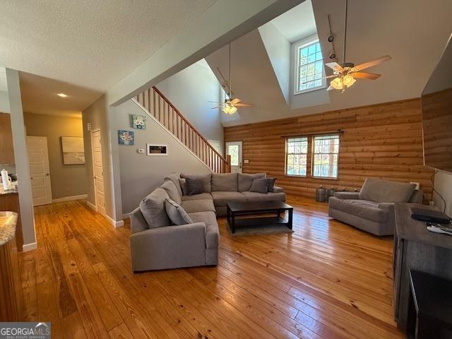 living room with light wood-style flooring, log walls, high vaulted ceiling, and ceiling fan