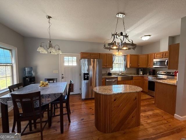 kitchen with dark wood finished floors, stainless steel appliances, a wealth of natural light, and an inviting chandelier