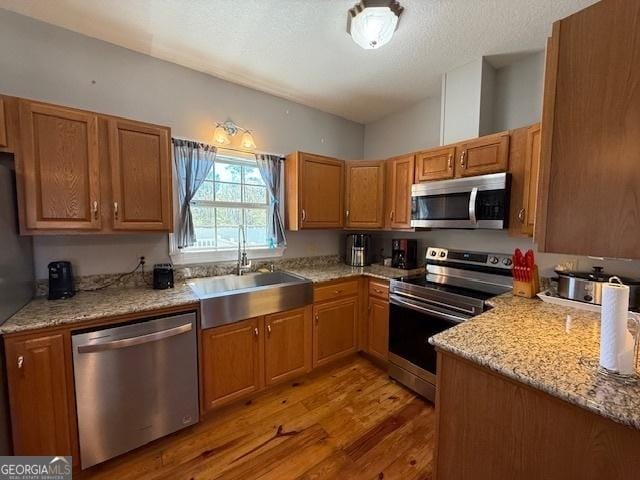 kitchen featuring light stone counters, light wood-style flooring, appliances with stainless steel finishes, a textured ceiling, and a sink