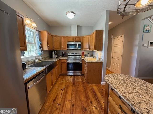 kitchen featuring light stone counters, dark wood finished floors, a sink, appliances with stainless steel finishes, and brown cabinets