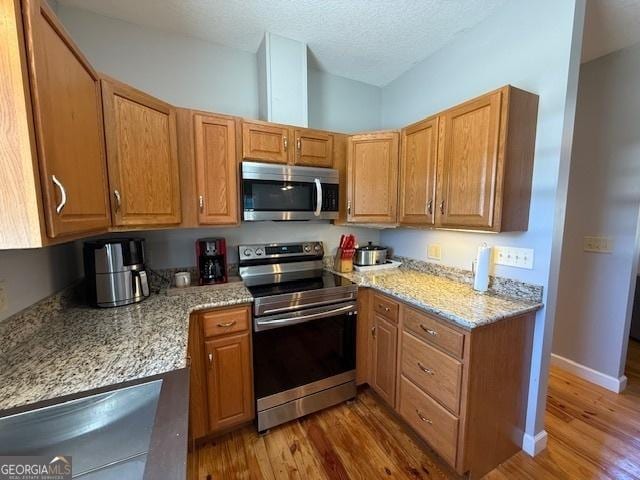 kitchen featuring light stone counters, wood finished floors, baseboards, appliances with stainless steel finishes, and a textured ceiling