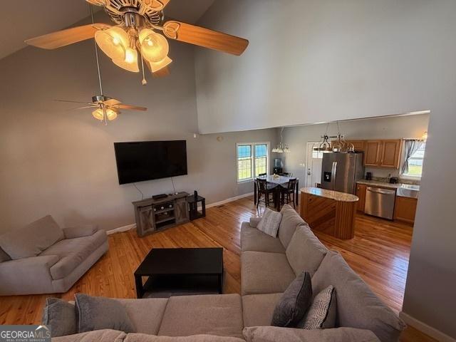 living room with baseboards, light wood-type flooring, a high ceiling, and a ceiling fan