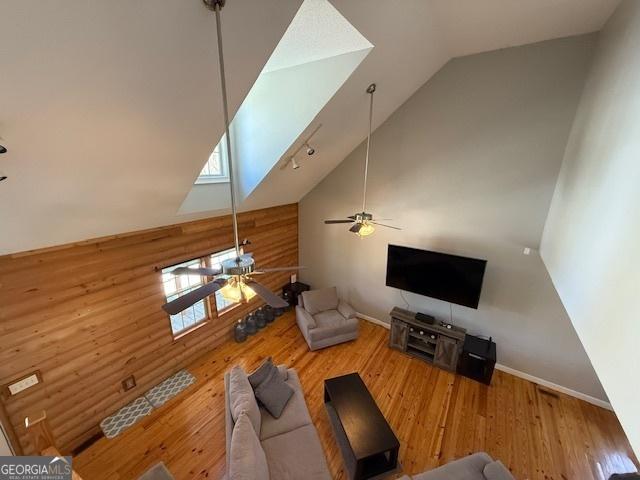 unfurnished living room with rustic walls, high vaulted ceiling, a ceiling fan, and wood finished floors
