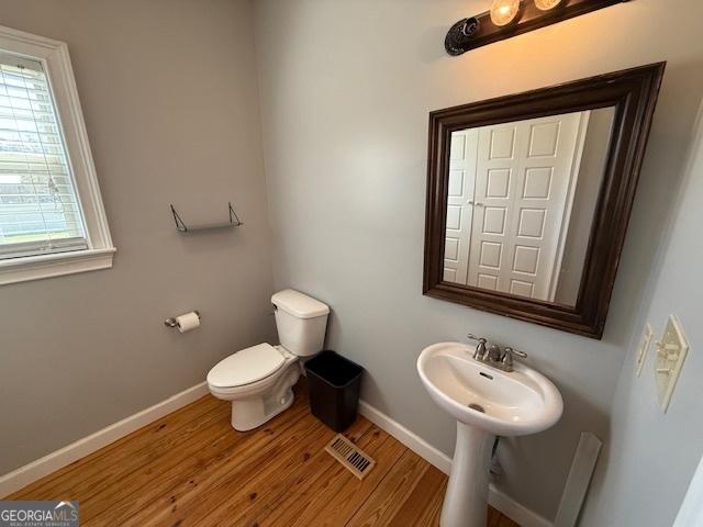 half bathroom with visible vents, toilet, a sink, wood finished floors, and baseboards