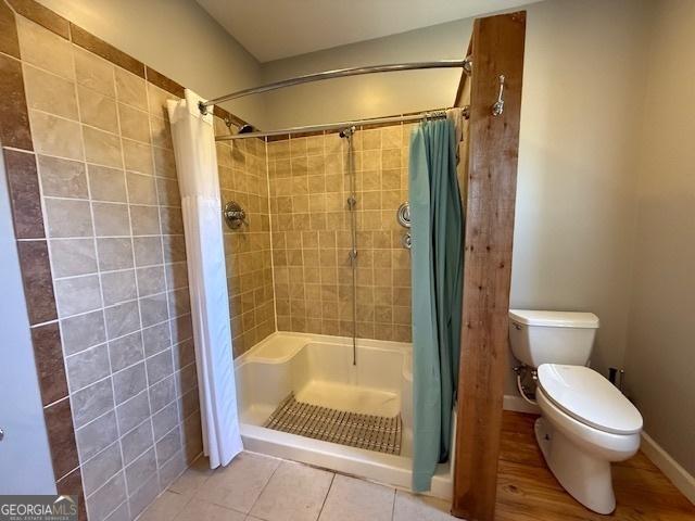 bathroom with tile patterned floors, toilet, baseboards, and a stall shower