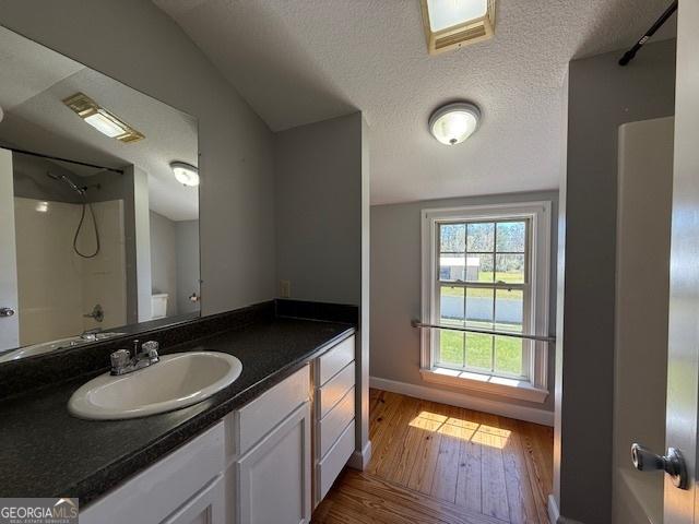 bathroom with vanity, washtub / shower combination, wood finished floors, baseboards, and a textured ceiling