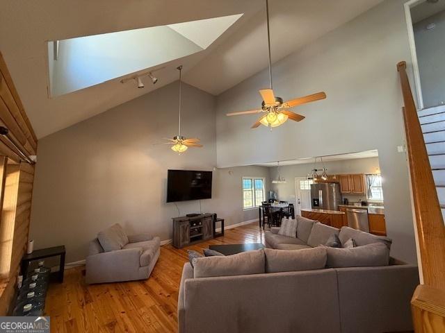 living area featuring lofted ceiling, light wood-style flooring, baseboards, and ceiling fan