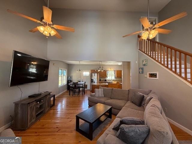 living room with baseboards, light wood-style flooring, and ceiling fan with notable chandelier
