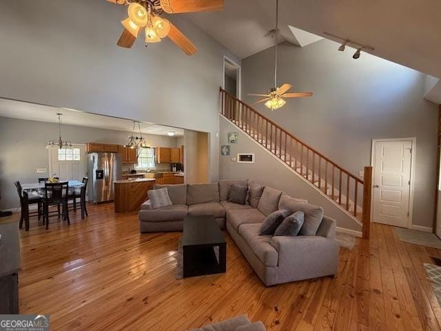 living room with stairway, light wood-style floors, high vaulted ceiling, and ceiling fan