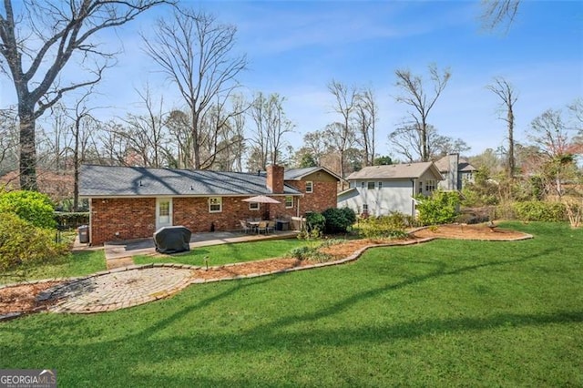 back of property with a patio, a yard, brick siding, and a chimney