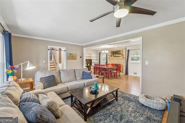living room featuring ceiling fan with notable chandelier, ornamental molding, and wood finished floors