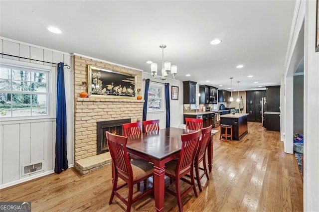 dining area with visible vents, an inviting chandelier, a fireplace, and light wood finished floors