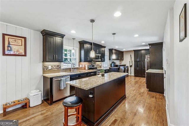 kitchen with light wood-style flooring, a sink, a center island, appliances with stainless steel finishes, and light stone countertops