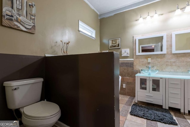 bathroom featuring toilet, ornamental molding, tile walls, wainscoting, and vanity