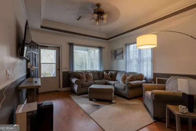 living room featuring a wealth of natural light, visible vents, a raised ceiling, and wood finished floors
