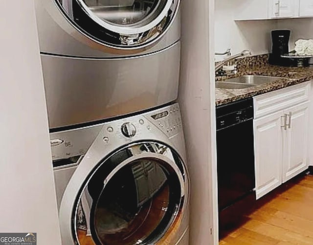 clothes washing area featuring a sink, laundry area, light wood finished floors, and stacked washer / drying machine