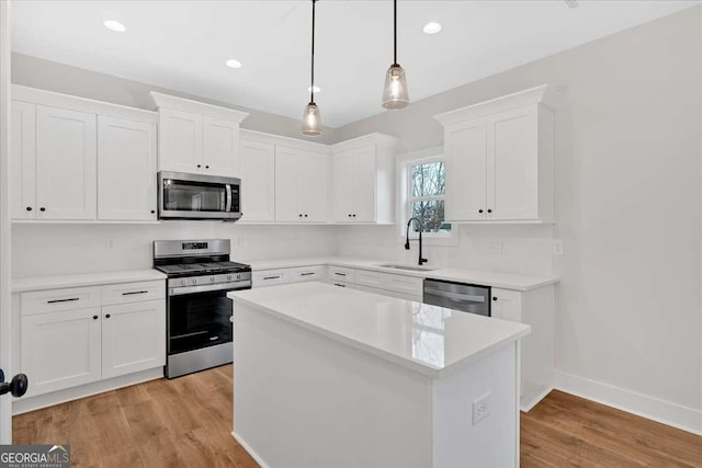 kitchen featuring light wood finished floors, white cabinets, appliances with stainless steel finishes, and a sink
