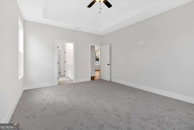 unfurnished bedroom with a tray ceiling, baseboards, carpet, and ensuite bathroom