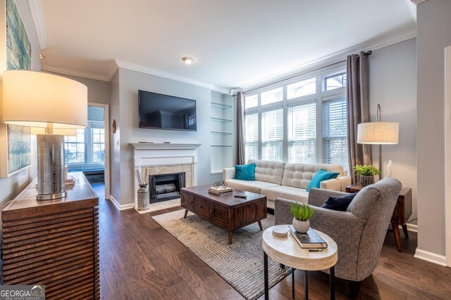 living room featuring a fireplace with flush hearth, dark wood-type flooring, built in features, crown molding, and baseboards