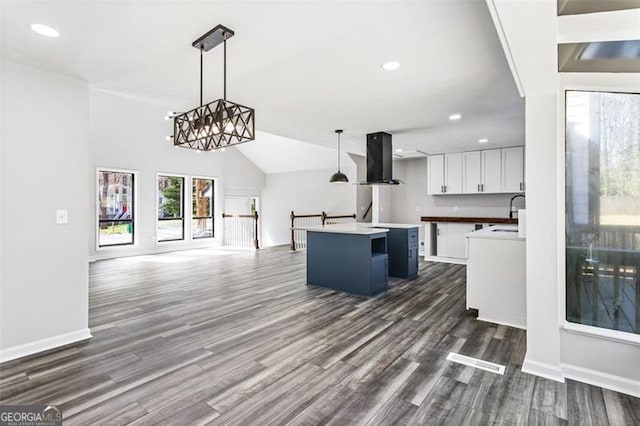 kitchen with exhaust hood, dark wood-type flooring, decorative light fixtures, a kitchen island, and white cabinetry