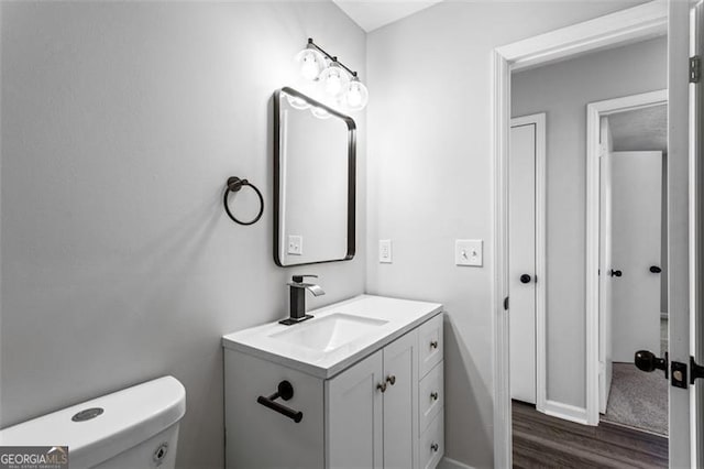half bath featuring wood finished floors, toilet, vanity, and baseboards