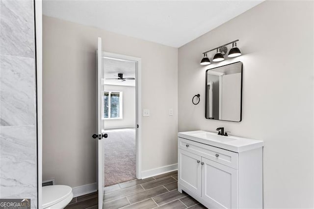 bathroom featuring toilet, wood tiled floor, vanity, and baseboards