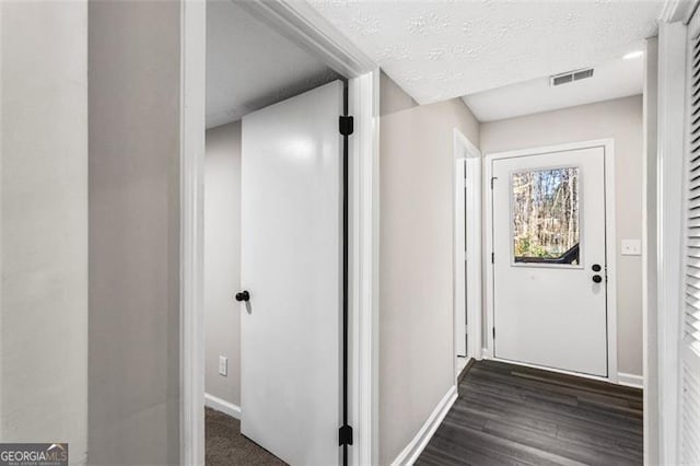 hall with dark wood-type flooring, a textured ceiling, visible vents, and baseboards