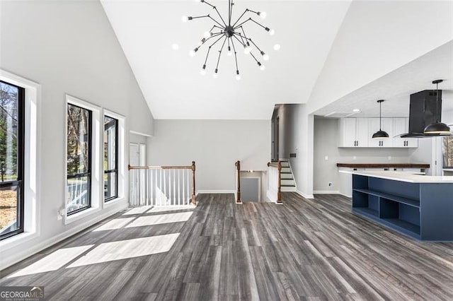 unfurnished living room with dark wood finished floors, high vaulted ceiling, a notable chandelier, and baseboards