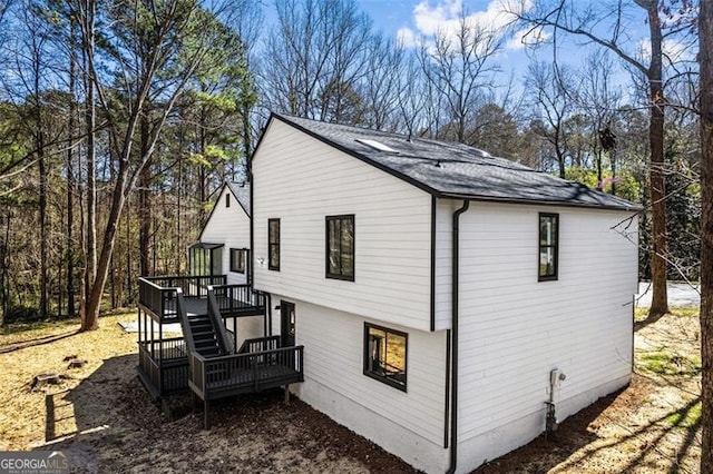 view of side of property with a deck, stairs, and roof with shingles