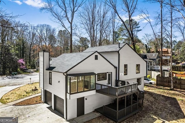 back of property featuring a chimney, a wooden deck, driveway, and an attached garage