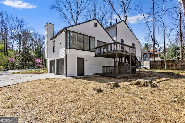 rear view of property featuring a sunroom, a chimney, a deck, an attached garage, and fence